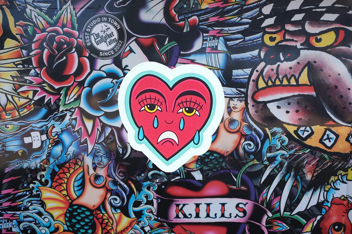 Color full image of tattoos that includes, mermaids, a bulldog head, a rose and other traditional tattoos. In the center there is a heart with a face that is crying.